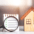 Image of small house replica next to a small note pad and magnification glass over a checklist.