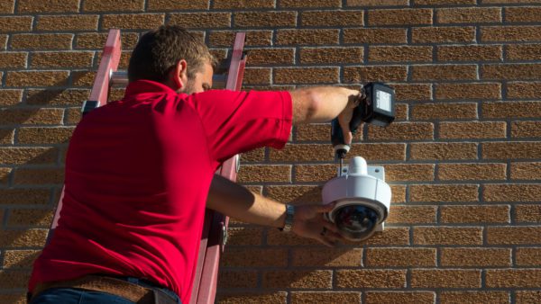 eps technician putting up a camera on the side of a brick building