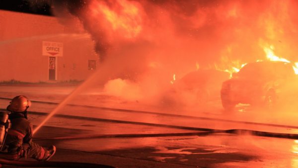 Firefighter putting out burning car in a parking lot at night.