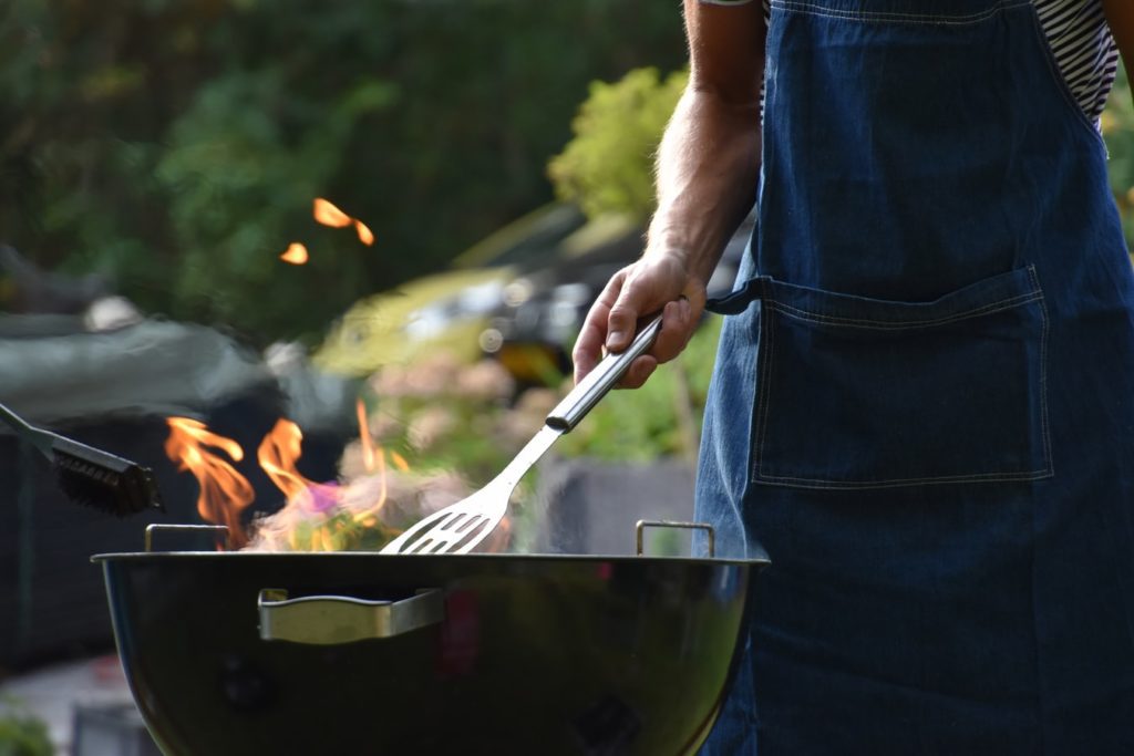 man with apron grilling on a charcoal grill
