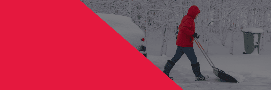 A young man shoveling a driveway in a red coat with a snowy car and trash bin in the background.