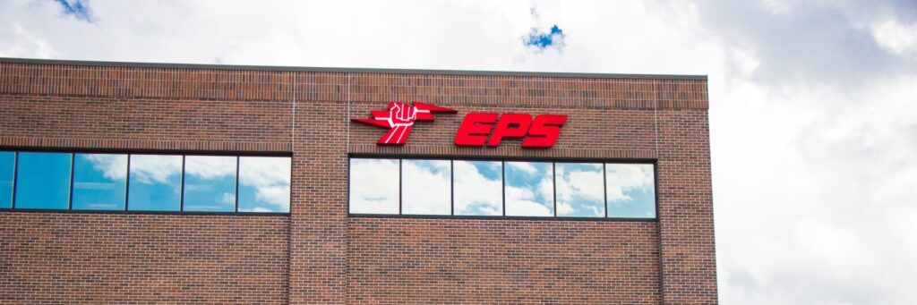EPS Security sign on the outside of the brick headquarters building, showind the top left corner, the sky, and the skies reflection in the windows.
