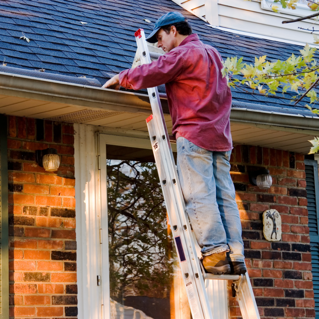 Man on a ladder cleaning the gutters on a home