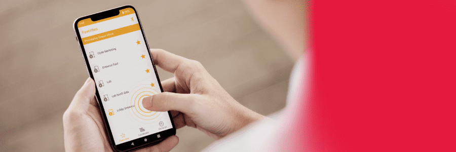 Over-the-shoulder view of a man on his phone with the cloud based access control PDK app open. He is clicking on "lobby entrance". Other rooms and entryways are displayed on his phone.